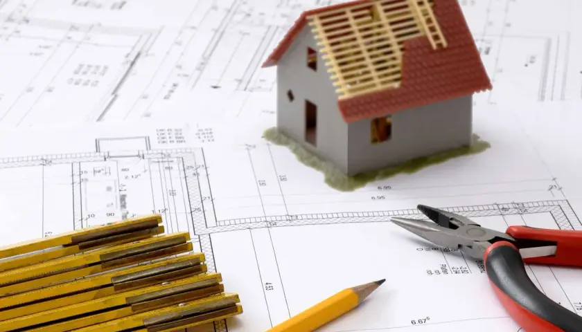 Ritningar för ett passivhus, en modell av ett hus, tumstock och tång. Planering för energieffektiva hem.
