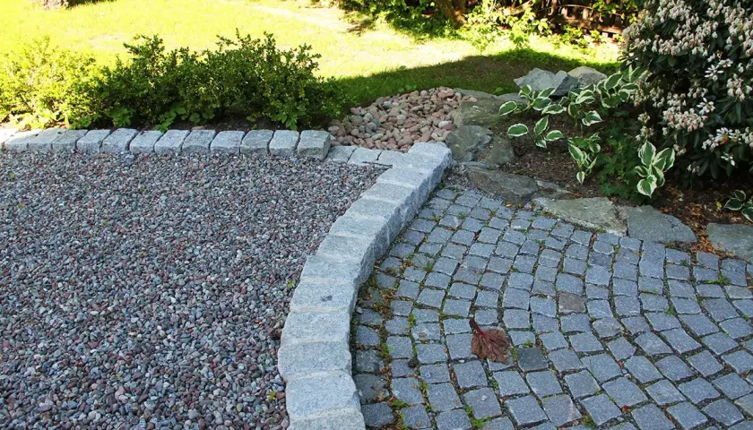 En vacker grusgång entre med stenläggning och kantsten. Gräsmattan och buskar i bakgrunden.