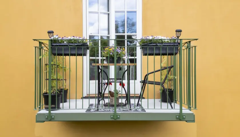 En charmig balkong, byggd på stolpar, med blomlådor, ett litet bord och stolar.