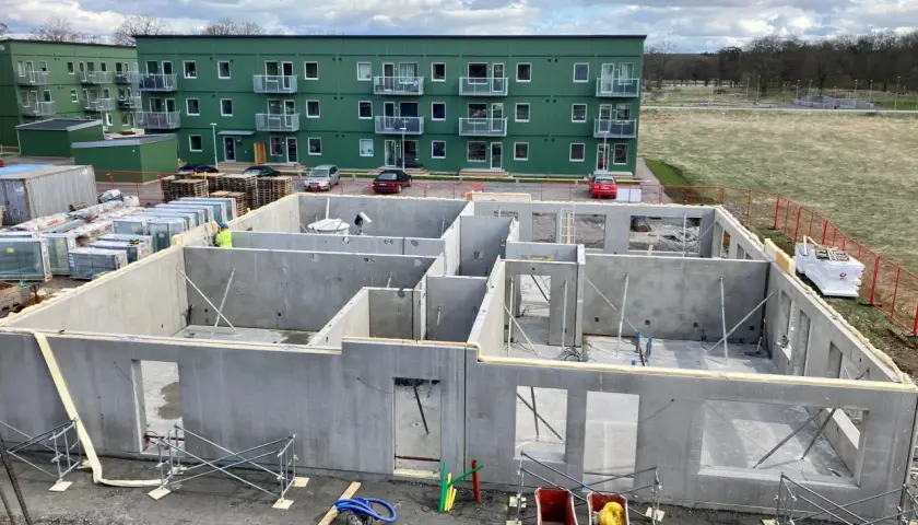 Grunden till ett hus byggs med prefabricerade betongelement. I bakgrunden syns gröna flerfamiljshus.