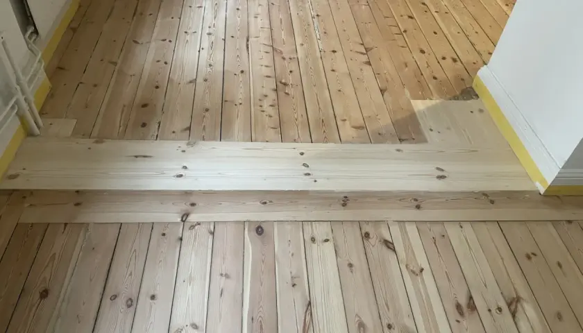 Renovering av ett gammalt trägolv, troligen från 30-talet, med nya plankor som lagts in för att ersätta skadade delar.