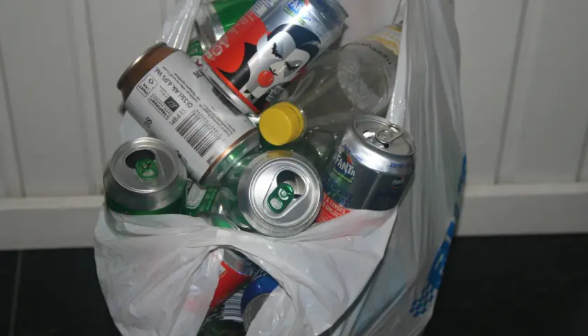 En plastpåse fylld med tomma burkar och flaskor, redo för pant. Här finns bland annat Fanta, ölburkar och en flaska med gul kork.