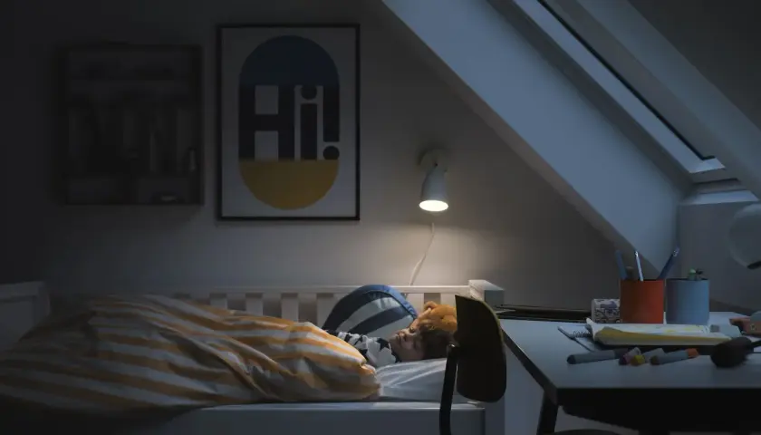 Barn sover i säng med randigt täcke. En lampa lyser över skrivbordet. God ventilation sovrum krav är viktigt för en god natts sömn.