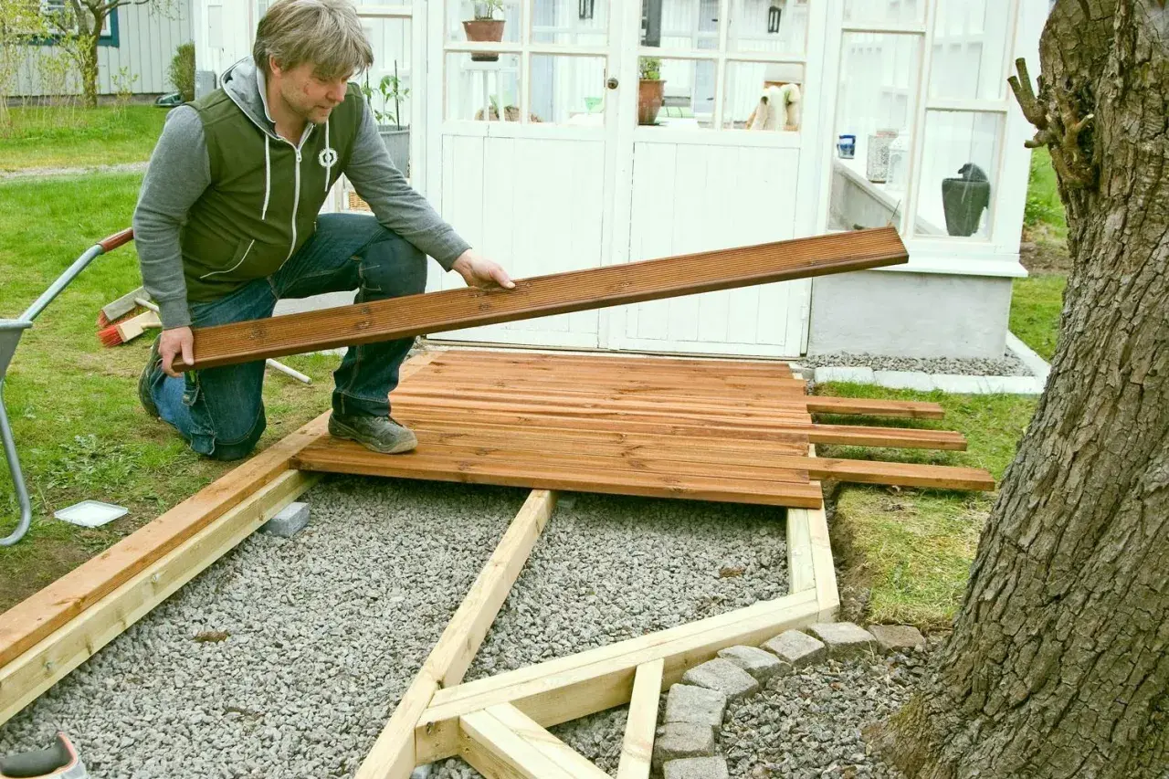 Man lägger trallbrädor för att underhåll altan. Ett nytt trädäck tar form vid växthuset.