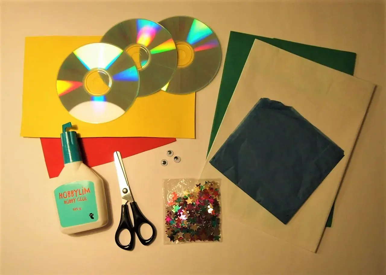 Här är material för att pyssla med gamla CD-skivor: lim, sax, glitterstjärnor, papper i olika färger och två små ögon.