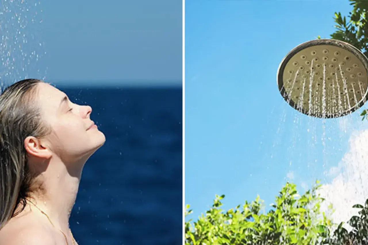 En kvinna njuter av en utedusch med insynsskydd av grönska. Vatten strömmar från en duschmunstycke mot en klarblå himmel.
