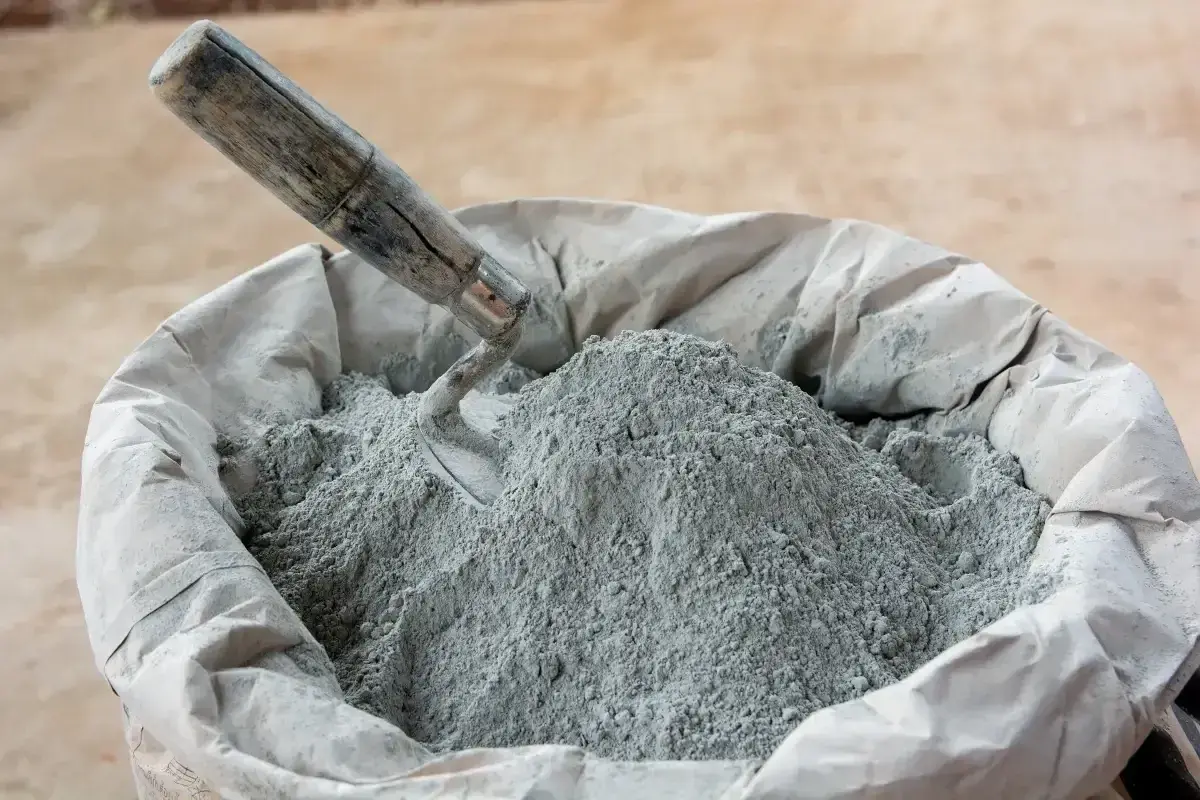 En säck med cement och betong, en murslev vilar i den gråa pulvret, redo för byggprojekt.