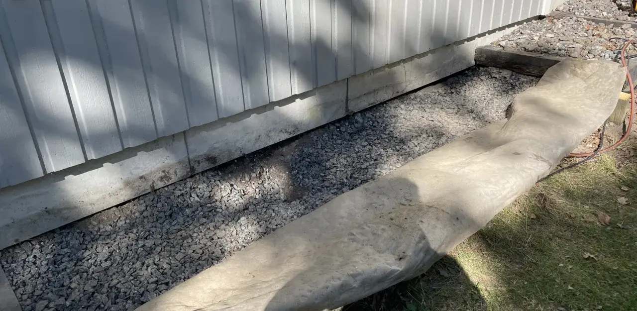 Grå makadam fyller utrymmet under husets grund, en del av arbetet med att bestämma hur mycket makadam under platta som behövs för dränering.