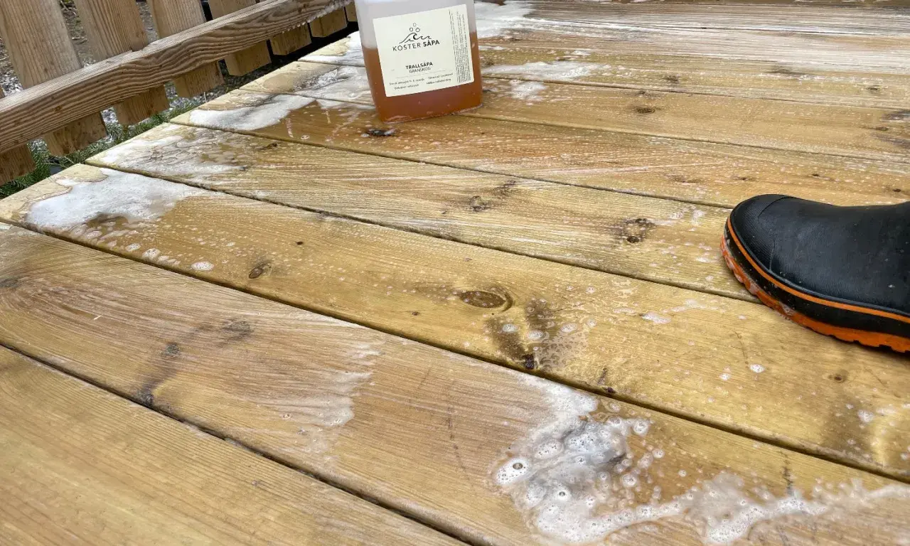 Rapssåpa gör altanen ren och fräsch. En flaska med såpa och en stövel på den skrubbade träaltanen.
