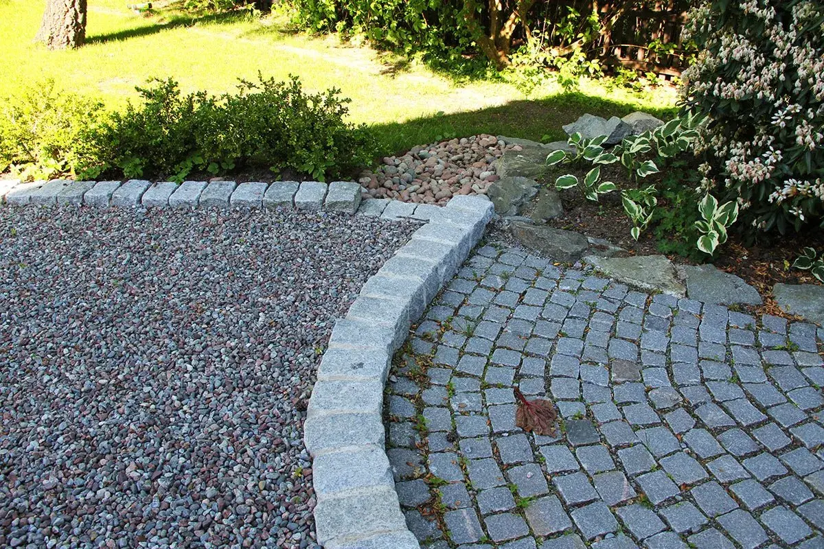 En vacker grusgång entre med stenläggning och kantsten. Gräsmattan och buskar i bakgrunden.