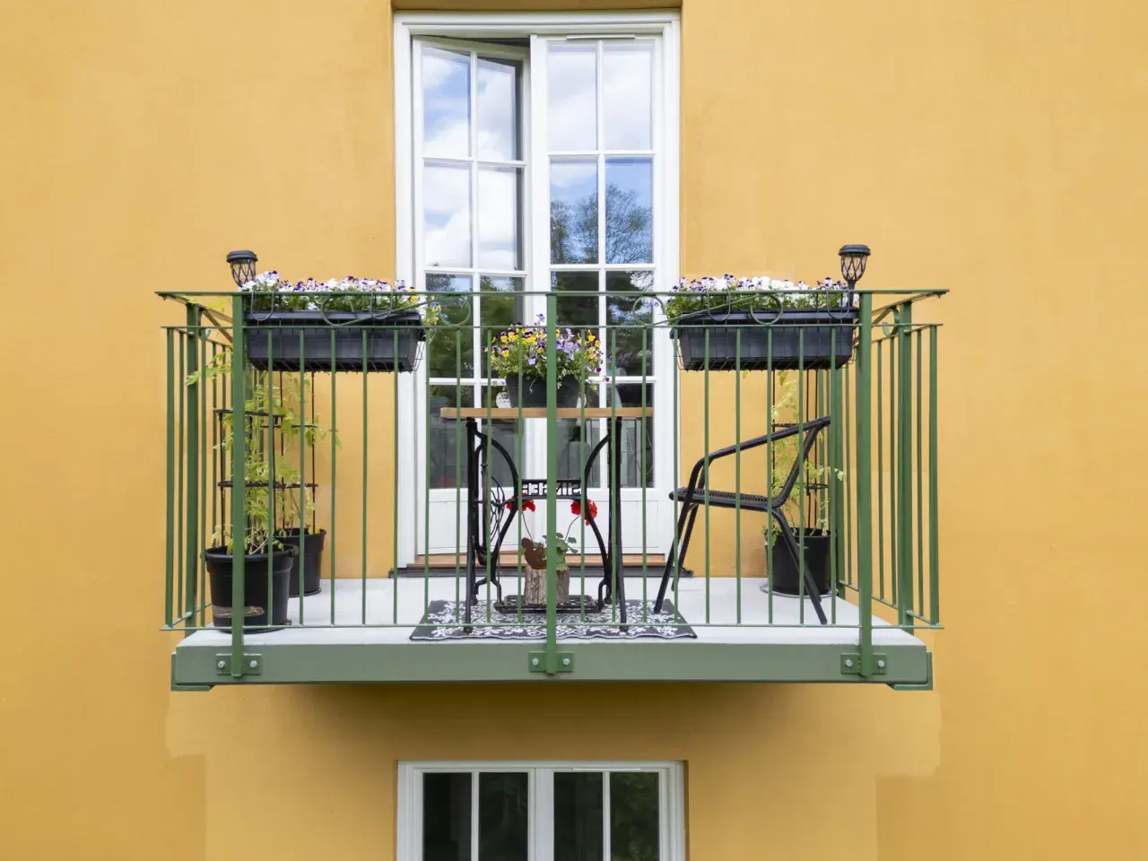 En charmig balkong, byggd på stolpar, med blomlådor, ett litet bord och stolar.