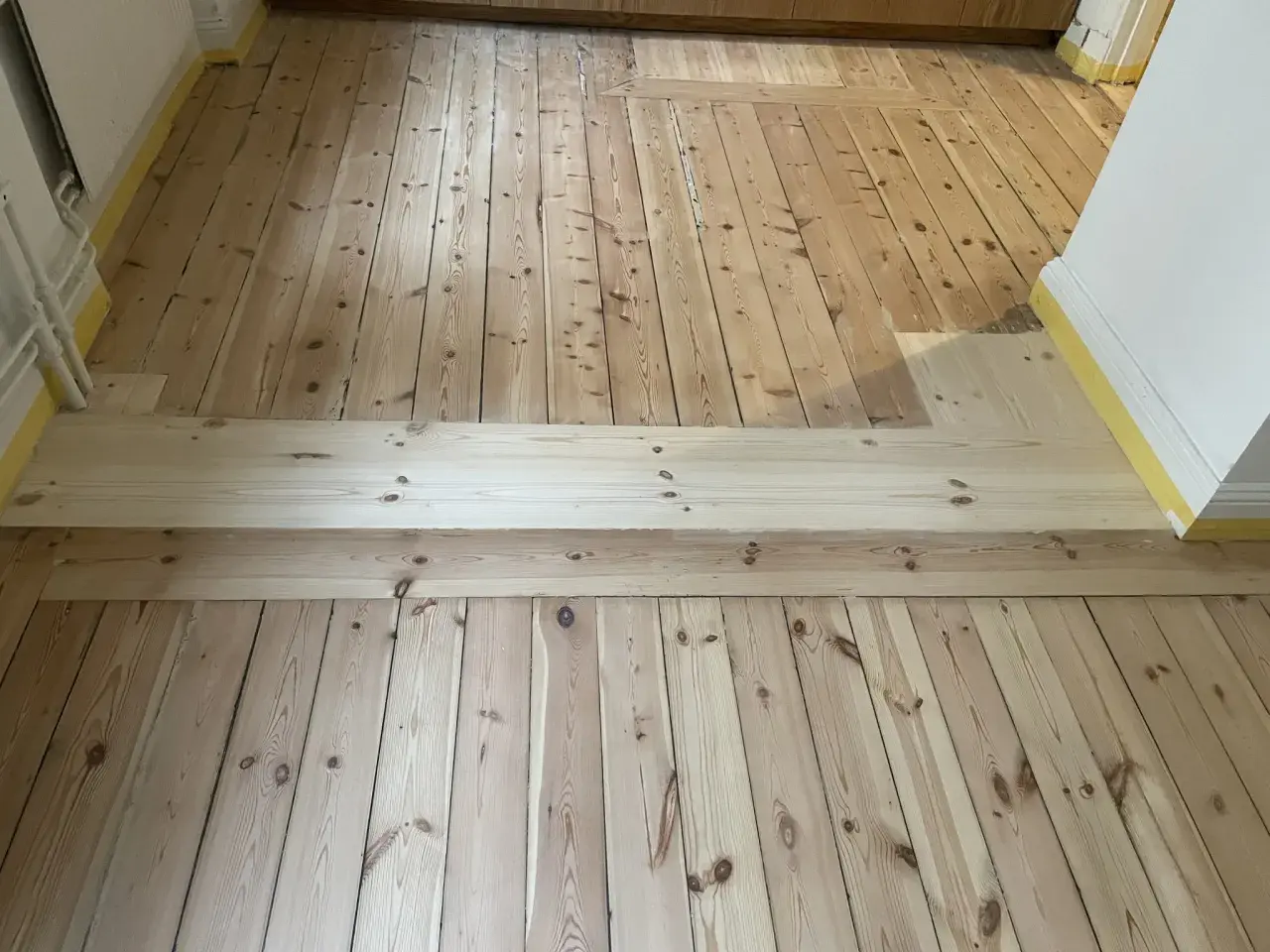 Renovering av ett gammalt trägolv, troligen från 30-talet, med nya plankor som lagts in för att ersätta skadade delar.