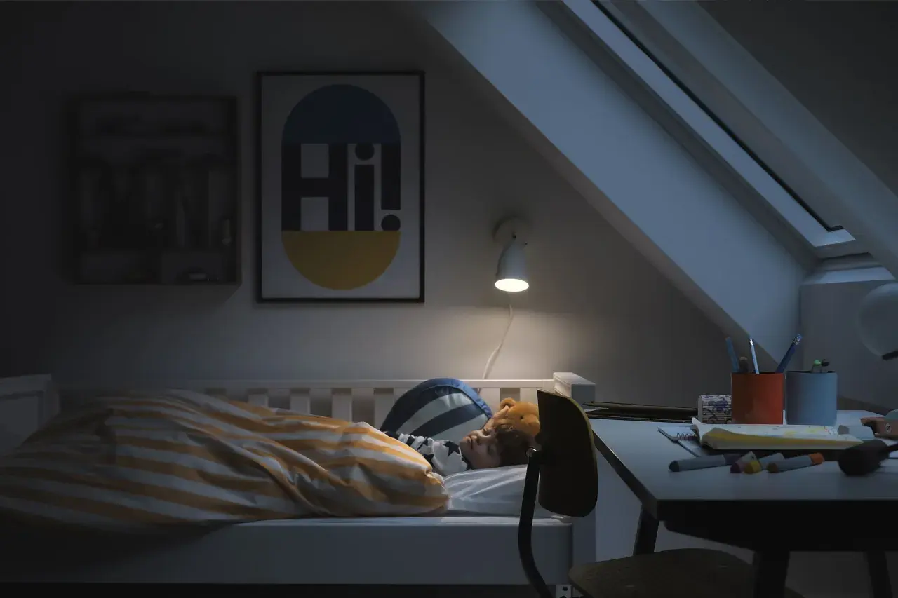 Barn sover i säng med randigt täcke. En lampa lyser över skrivbordet. God ventilation sovrum krav är viktigt för en god natts sömn.