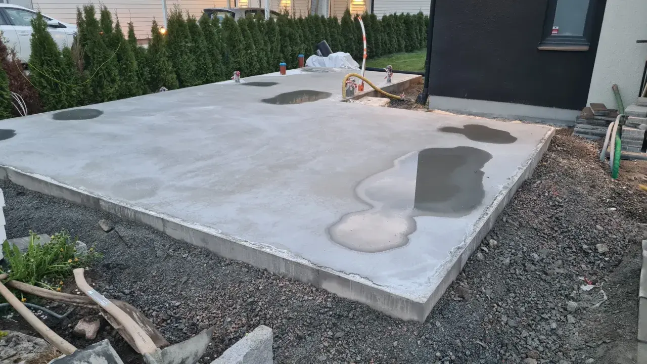 Nyligen gjuten betongplatta med vattenpölar, en påminnelse om att gjuta i regn kan vara utmanande.