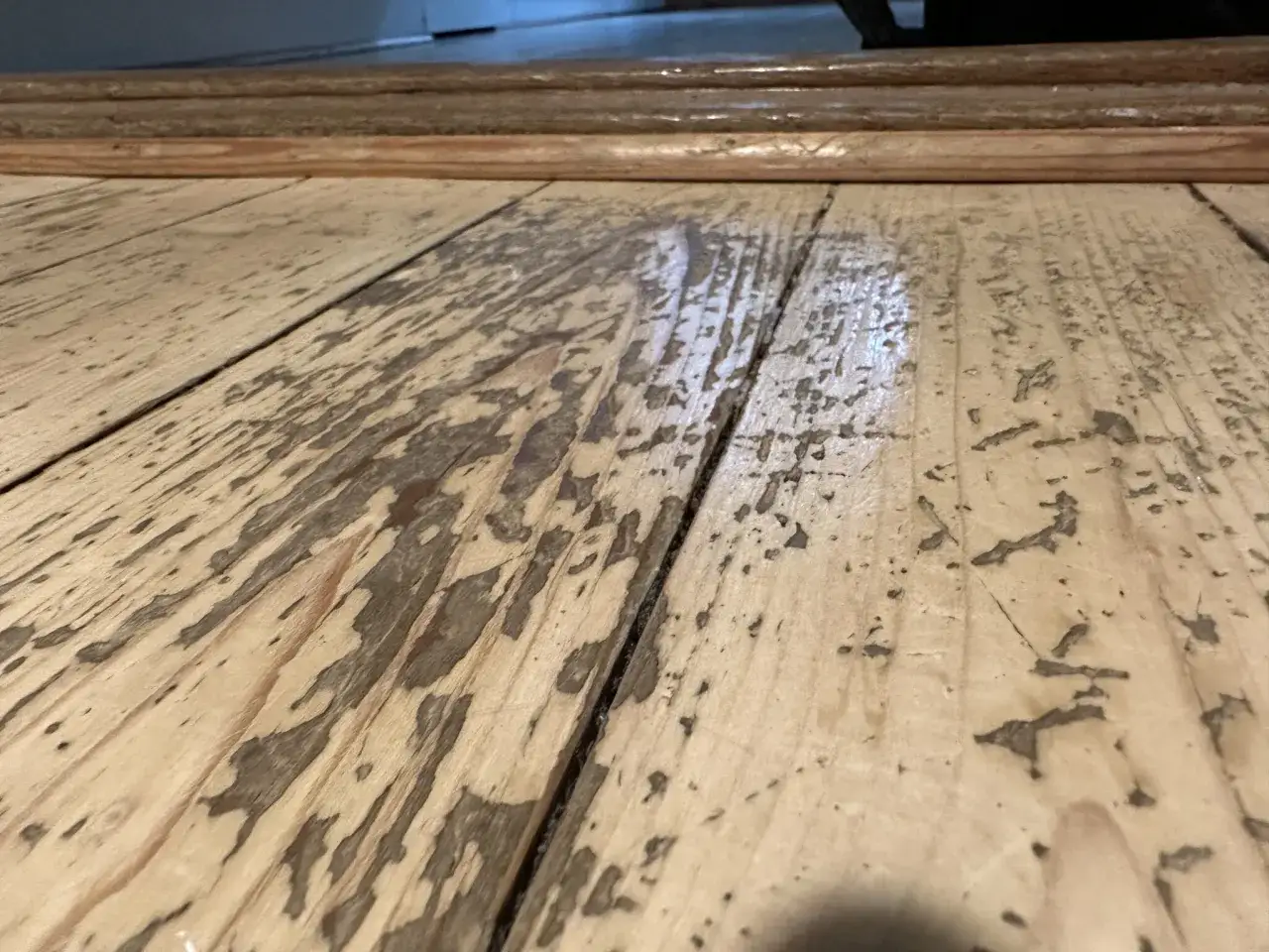 Ett slitet, gammalt plankgolv med synliga sp&aring;r av tid och anv&auml;ndning.