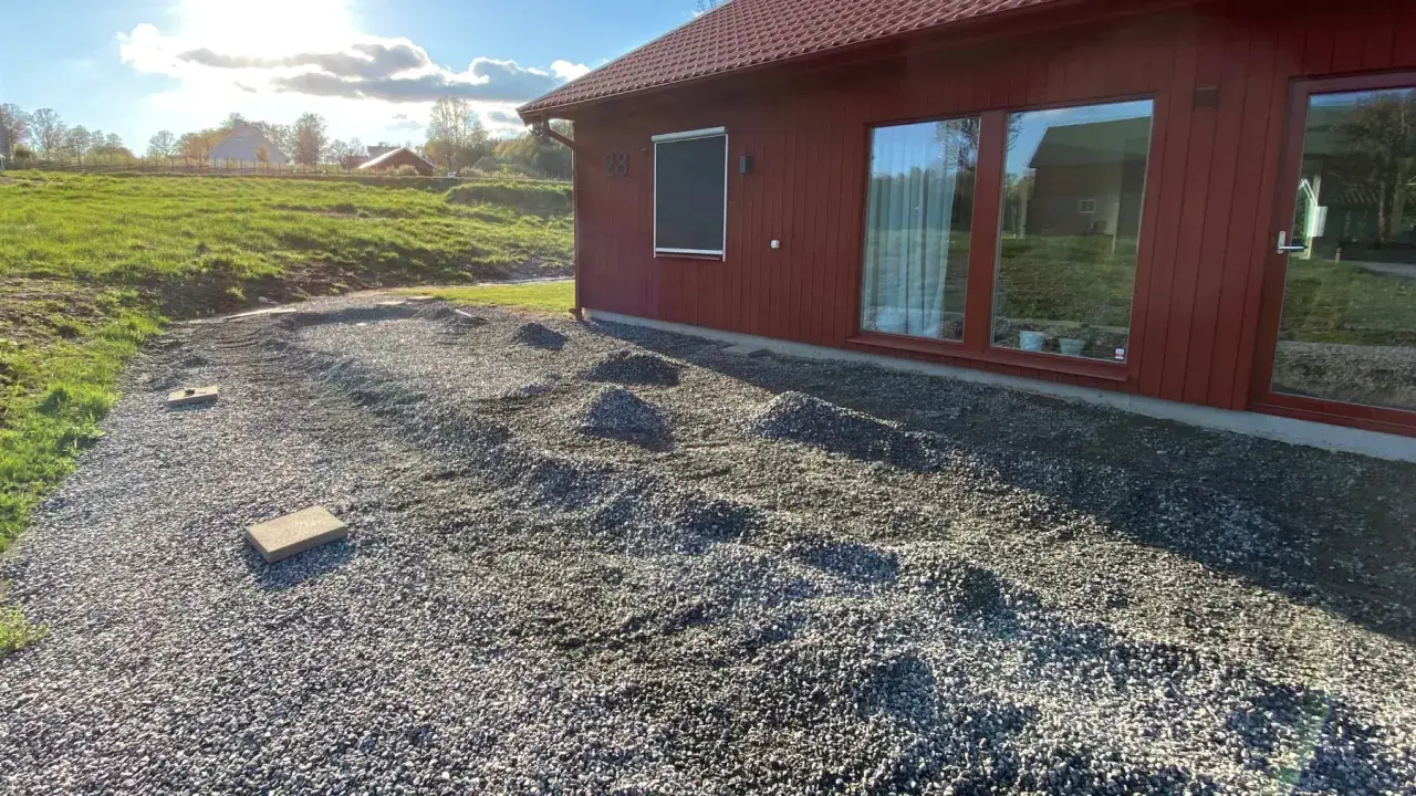 Grus under altan f&ouml;rbereds. Sm&aring; h&ouml;gar av grus ligger utspridda framf&ouml;r det r&ouml;da huset, redo att j&auml;mnas ut f&ouml;r en ny uteplats.