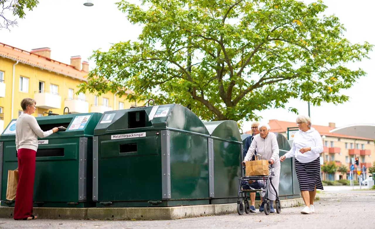 &Auml;ldre kvinnor sorterar sopor vid &aring;tervinningsstationer. En kvinna l&auml;gger i n&aring;got i en beh&aring;llare, medan tv&aring; andra g&aring;r f&ouml;rbi med en rollator.