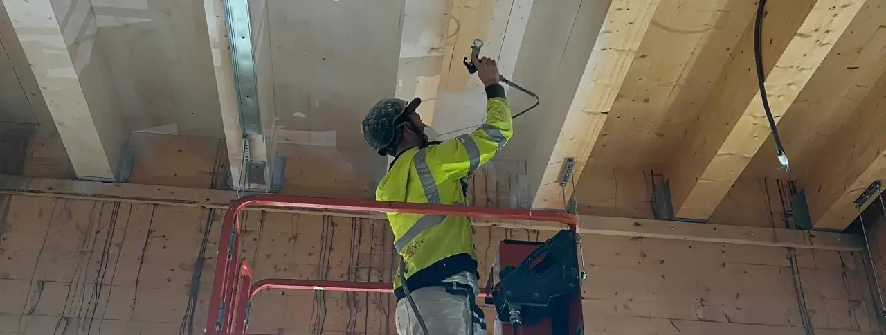Arbetare i lift sprutar brandskydd p&aring; tr&auml;bj&auml;lkar, f&ouml;ljer Boverkets byggregler f&ouml;r brandskydd.