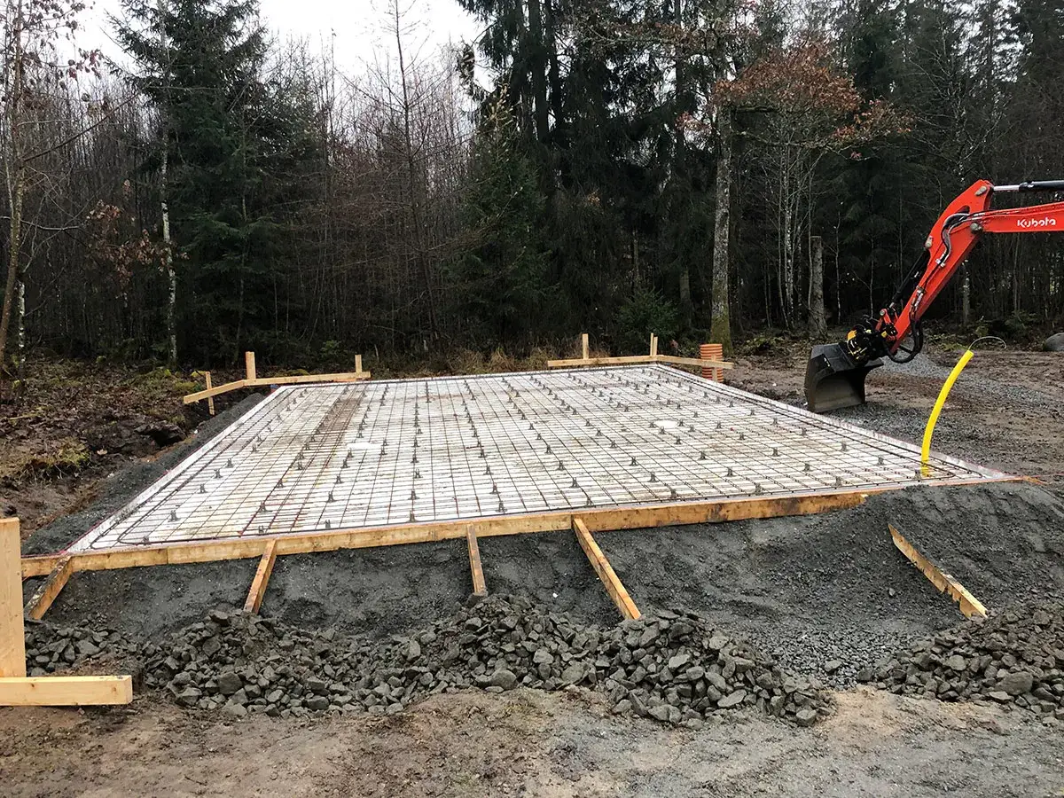 F&ouml;rberedelser f&ouml;r ett garage under mark. Armeringsj&auml;rn och formvirke p&aring; plats. En gr&auml;vmaskin syns i bakgrunden.