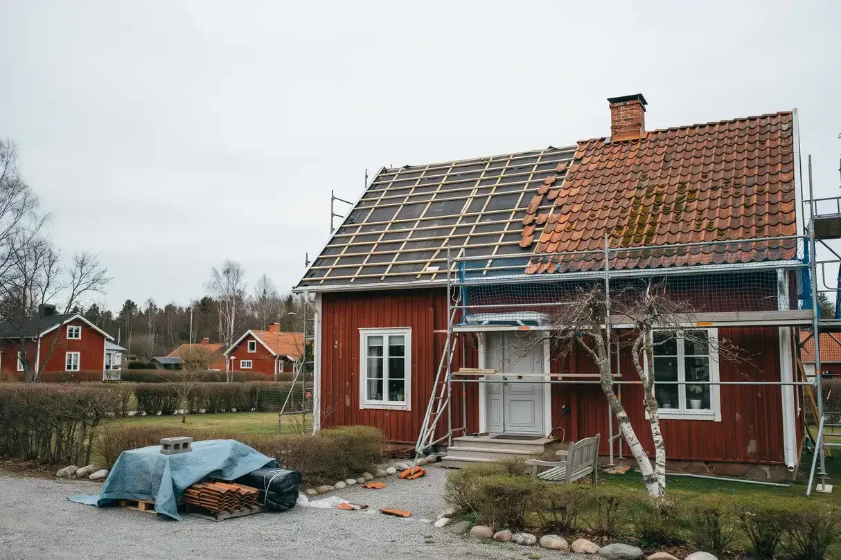 R&ouml;tt hus i Sverige med st&auml;llningar runt taket. Taket &auml;r under renovering, med nya takpannor som v&auml;ntar p&aring; att l&auml;ggas.