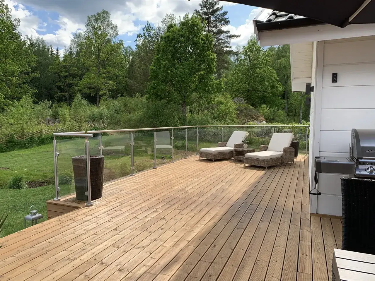 En nybehandlad trall i trä med solstolar och grill, omgiven av grönskande natur.