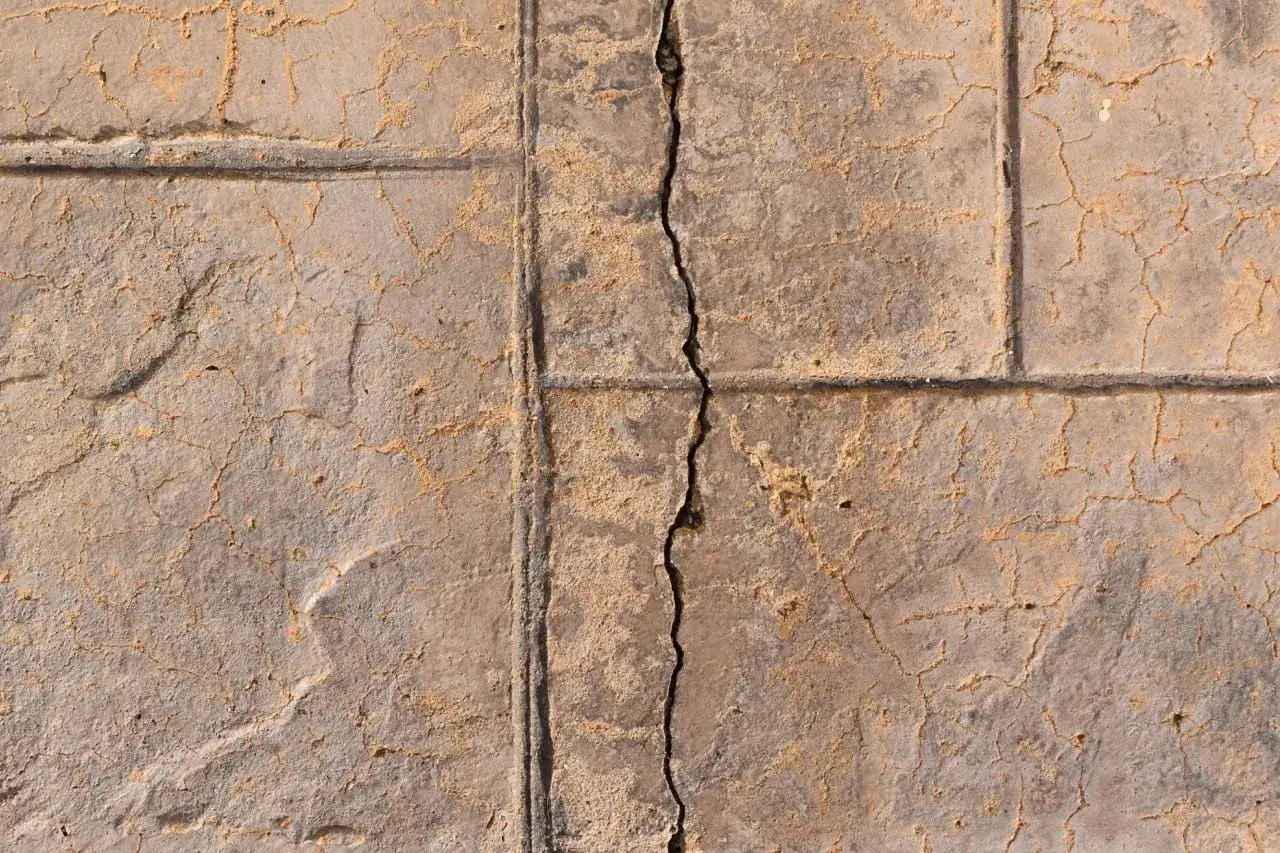 Detaljerad vy av betongplattor med synliga krympsprickor och sand i fogarna.