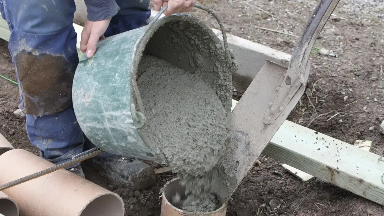 Hink med f&auml;rdigblandad betong h&auml;lls ner i ett r&ouml;r. En person i bl&aring; arbetskl&auml;der ser skillnad cement betong.