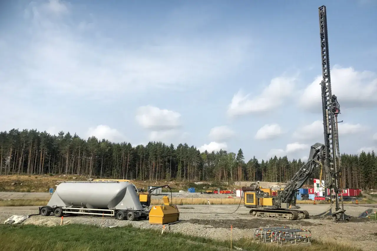 Stor borrigg, en tankbil och annan byggutrustning p&aring; en byggarbetsplats med skog i bakgrunden. Arbetet med kc pelare p&aring;g&aring;r.