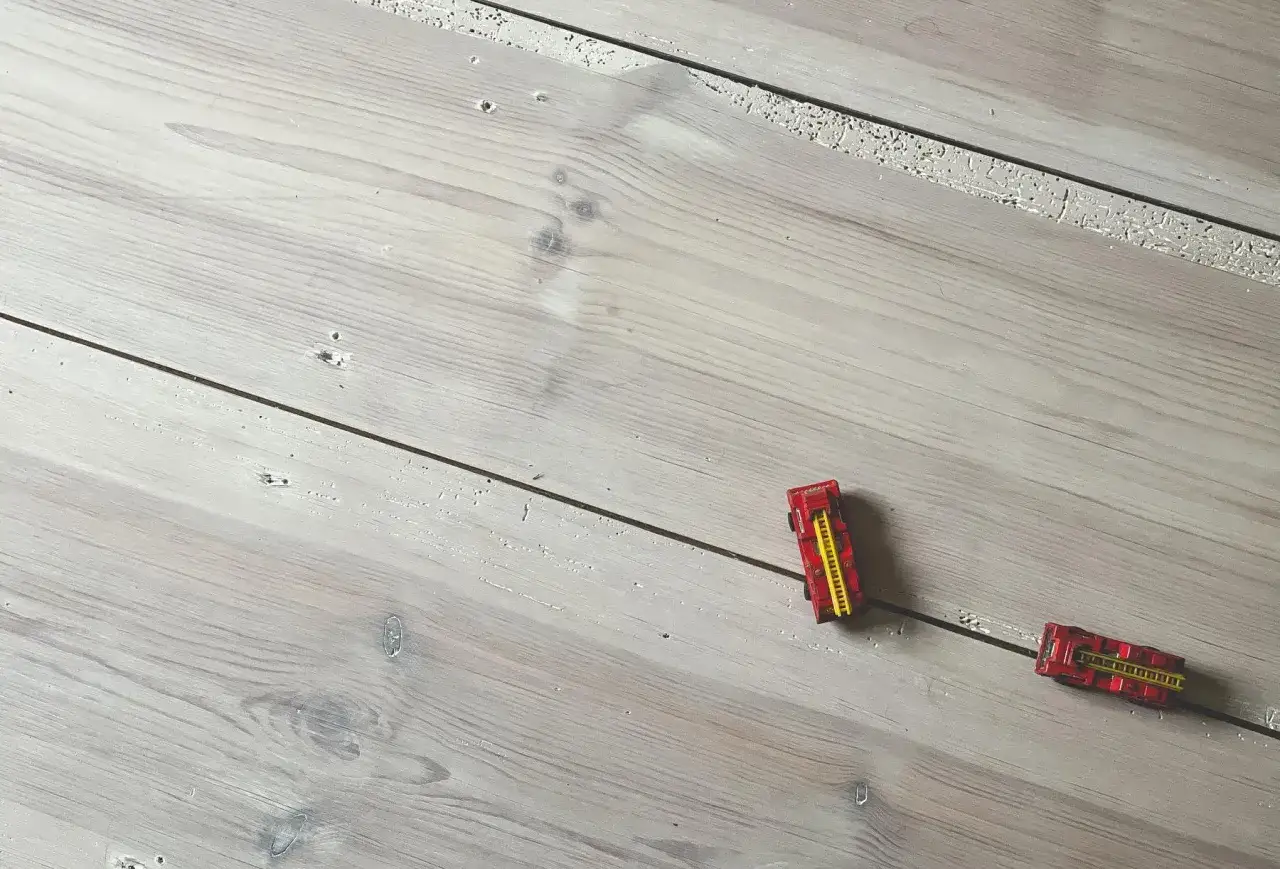 Tv&aring; leksaksbrandbilar k&ouml;r p&aring; ett lutat furugolv.