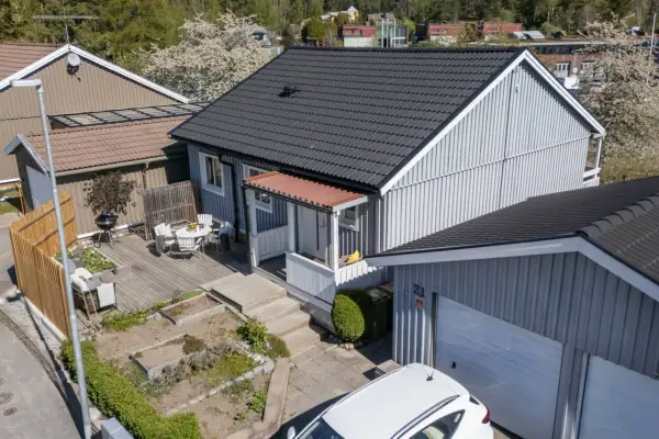 Ett charmigt hus med nummer bbr 21. Trädgårdsmöbler på altanen, en grill och en vit bil framför garaget.